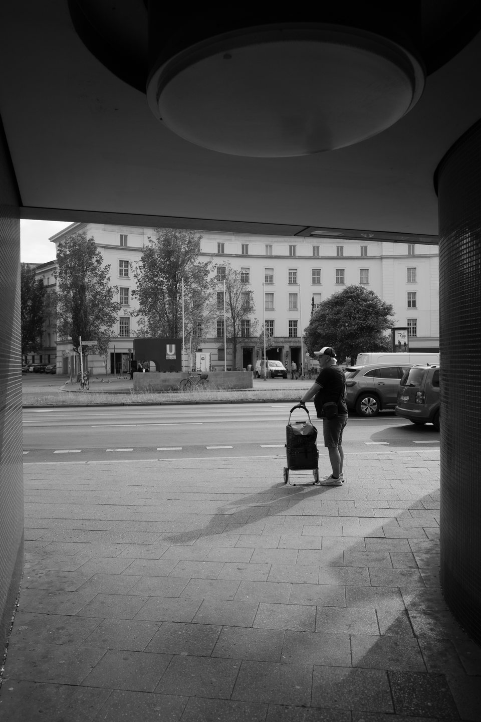 Two people with a shopping trolley waiting beside a street
