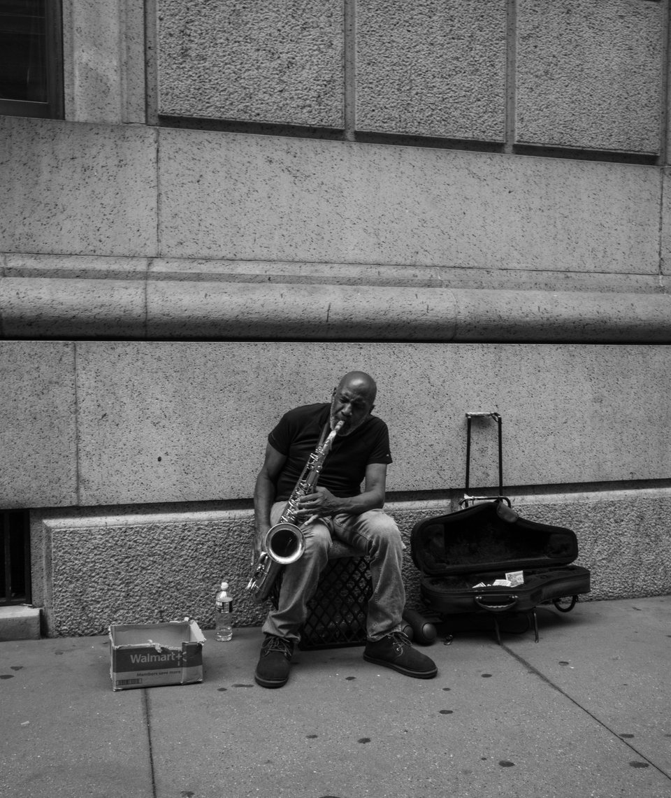 A street musician playing saxophone against a stone wall