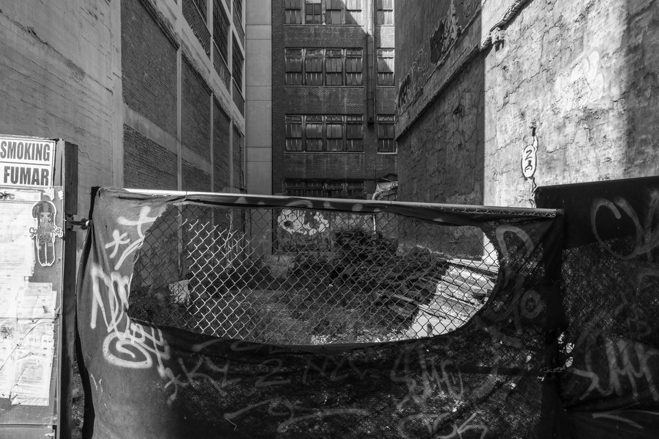 A worn sofa behind chain-link fencing in an alley