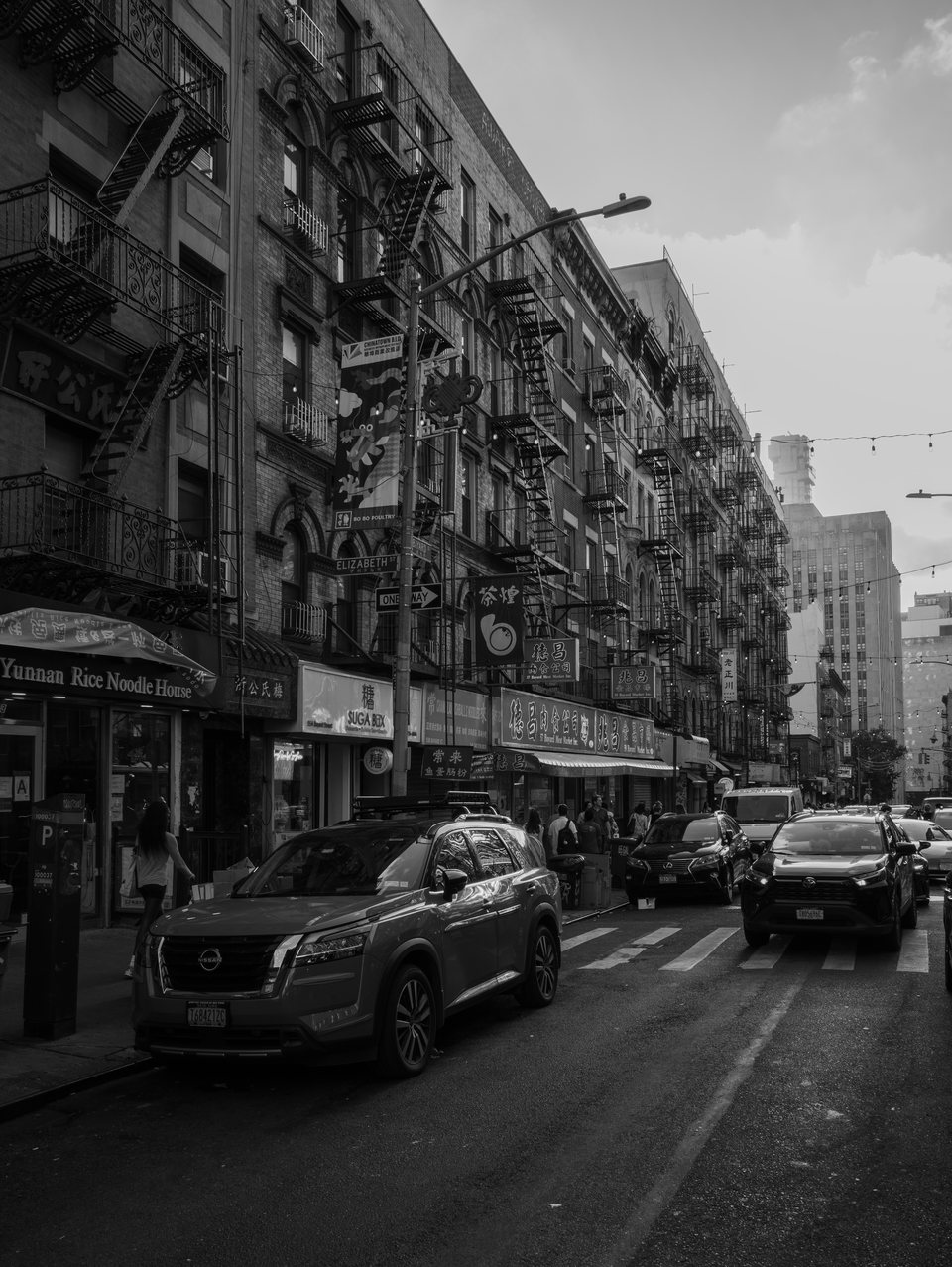 Traffic moving through a dense city street lined with fire escapes