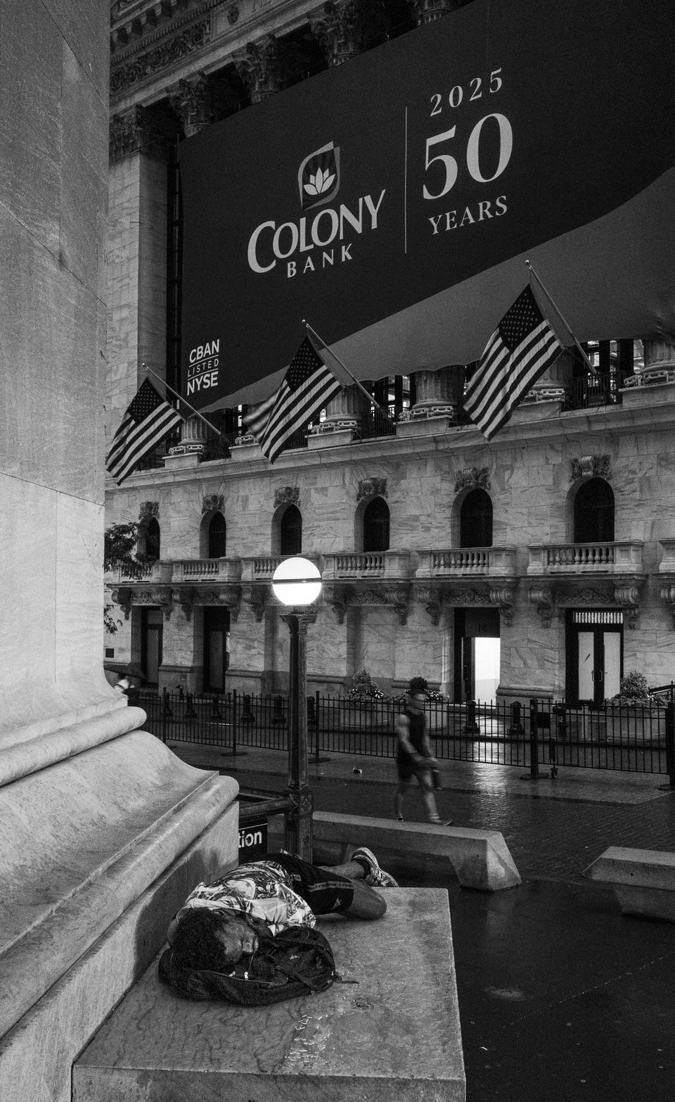 A person resting on a stone ledge below flags and a bank awning