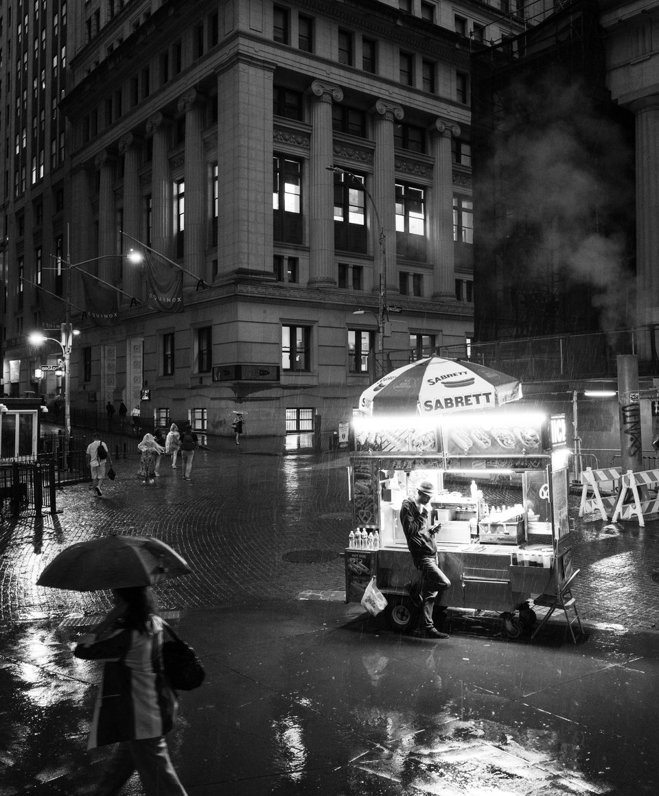 A food cart and umbrellas on a wet city corner at night