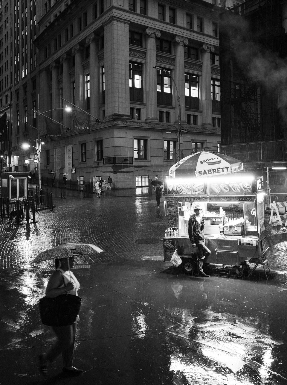 A glowing food cart reflected on a rain-soaked street at night