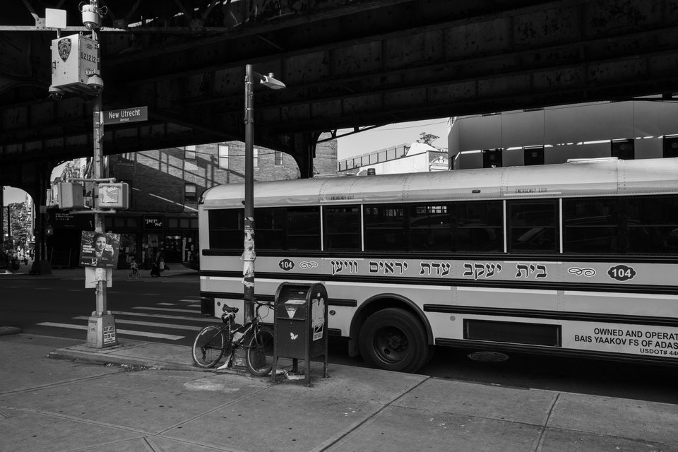 A city bus waiting at a curb beneath an elevated structure